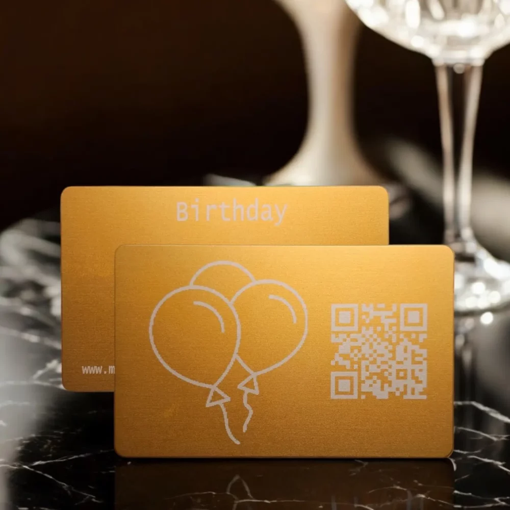 Geburtstags-Metallkarte mit Vorderseite, gravierten Luftballons und QR-Code, daneben die Rückseite mit graviertem Namen 'Birthday' und individueller Karten-ID