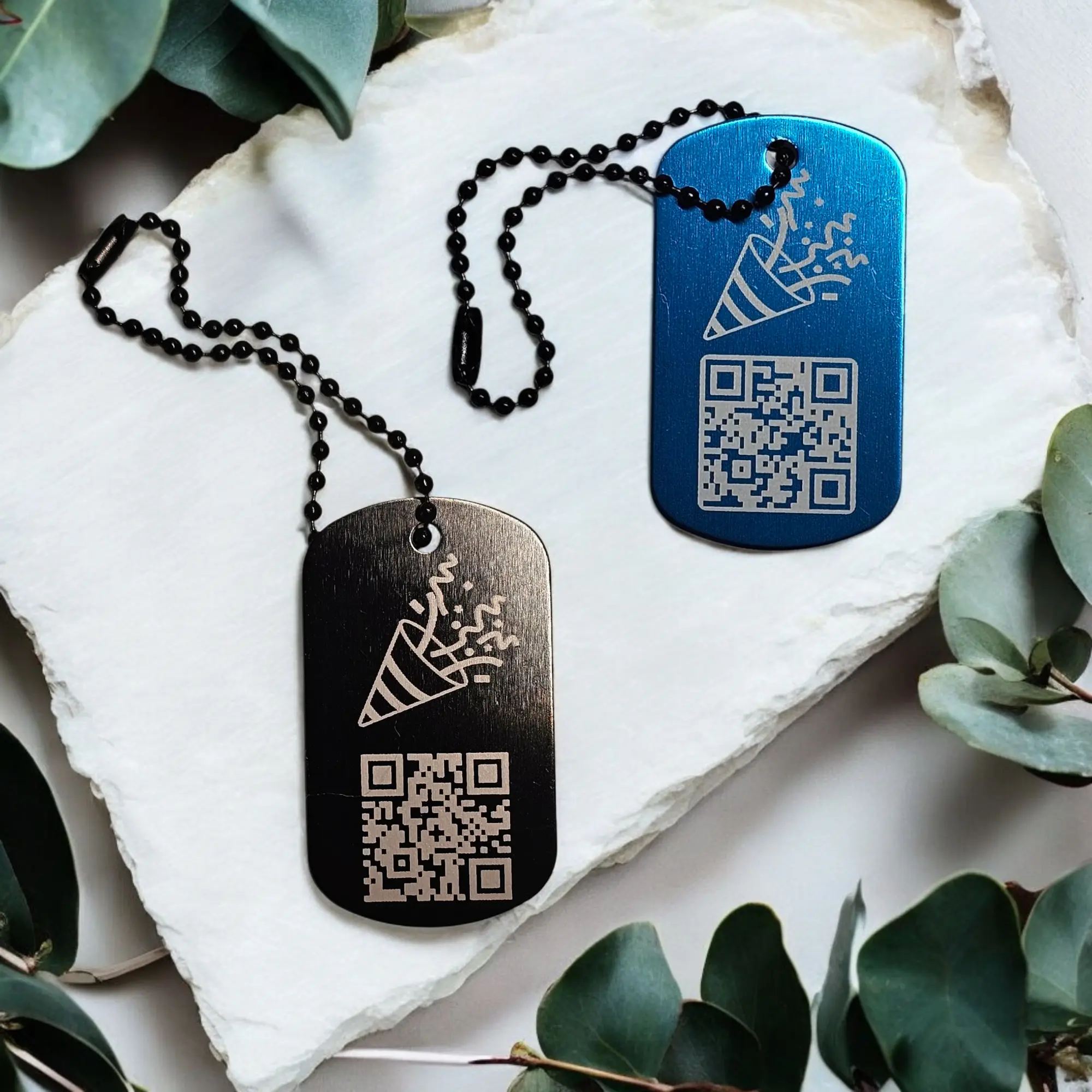 Zwei Party Popper Anhänger aus Metall in Schwarz und Blau mit graviertem QR-Code und Konfettimotiv – für digitale Botschaften zu besonderen Anlässen