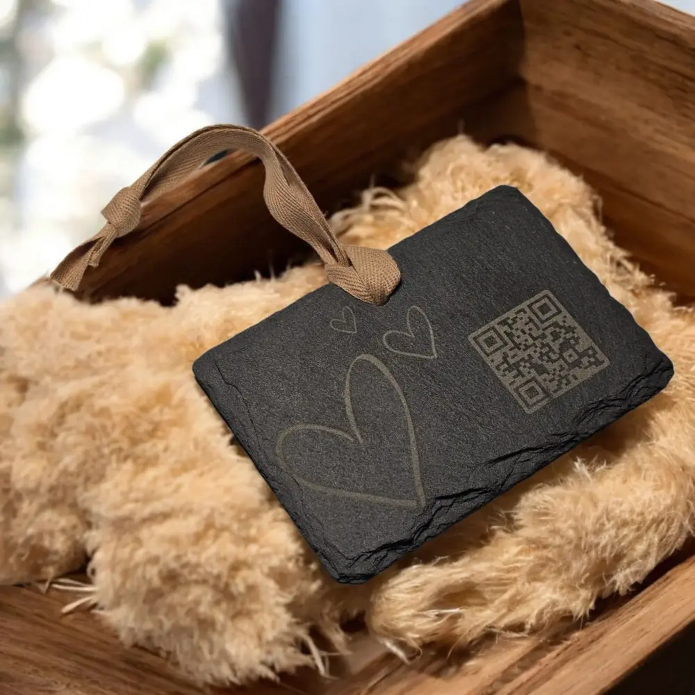 Der Schiefer-Anhänger „Love“ im Vintage-Holzkasten auf Naturfasern präsentiert, Herzmotiv und QR-Code klar erkennbar.