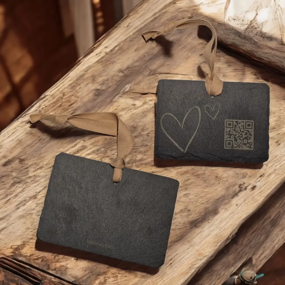 Zwei rechteckige Schiefer-Anhänger „Love“ mit QR-Code und Herzgravur auf rustikalem Holz, rückseitig „Monvou.com“ dezent gelasert.