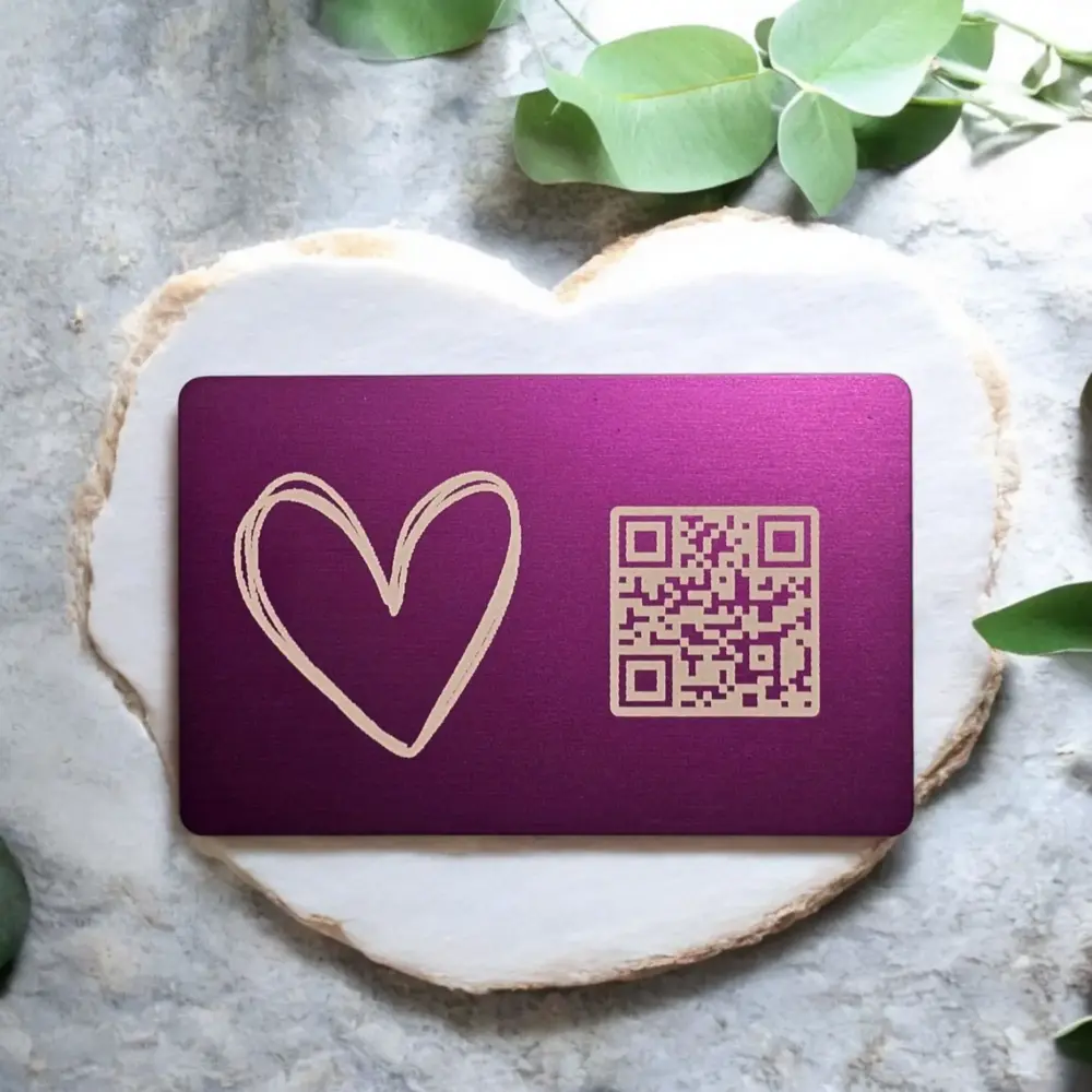 Herzförmige Metallkarte in Violett mit QR-Code auf weißem Schiefer – Geschenkidee von Monvou